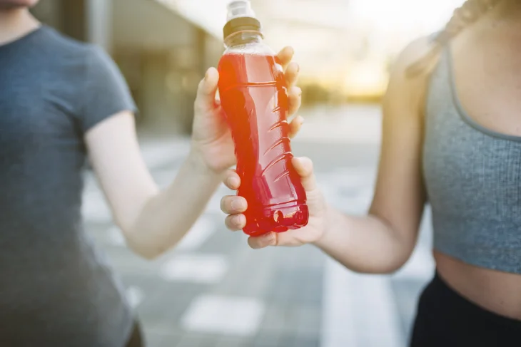 dos mujeres deportistas sosteniendo una bebida energética de color rojo que provoca un desgaste en esmalte dental