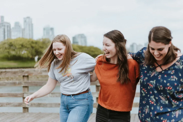Dolor de encías: amigas sonrientes caminando abrazadas al aire libre, reflejando bienestar tras tratamiento dental para aliviar molestias en las encías.